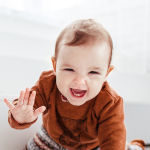 happy-child-orange-sweater-plays-with-feather-floor